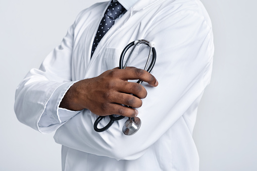Cropped of african american doctor with arms crossed holding stethoscope over white studio background
